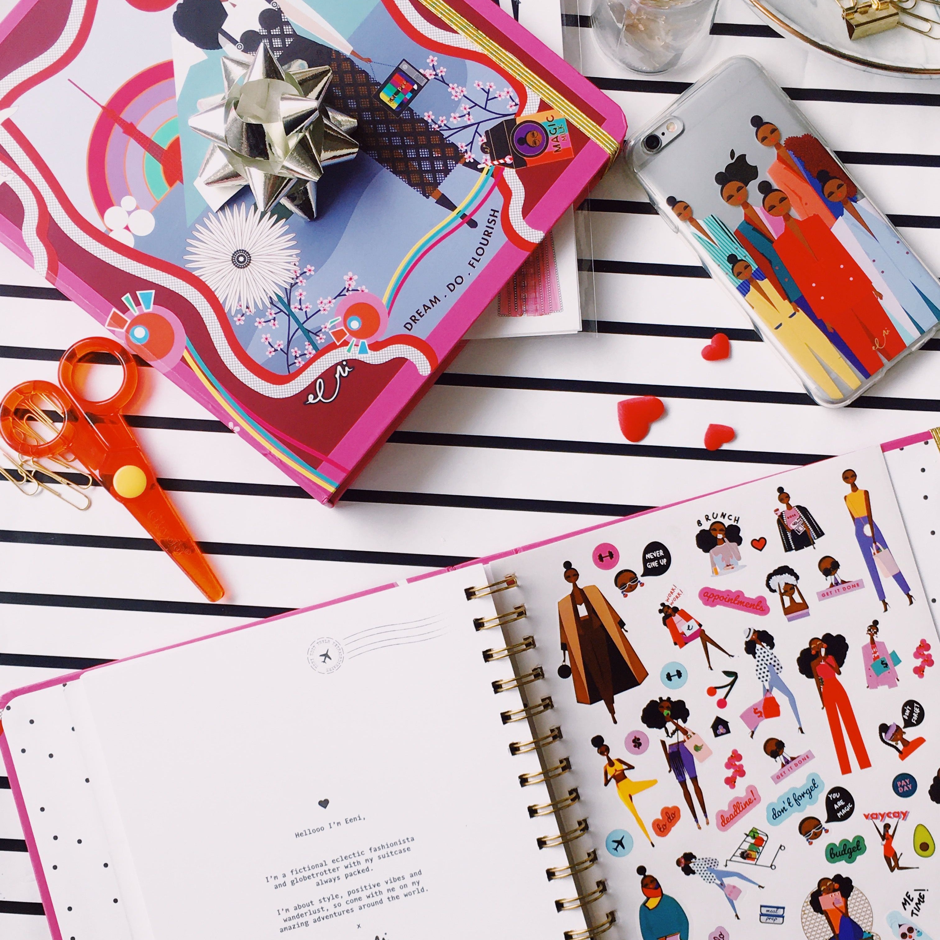 Open notebook with illustrated pages on a striped surface with stationery items.